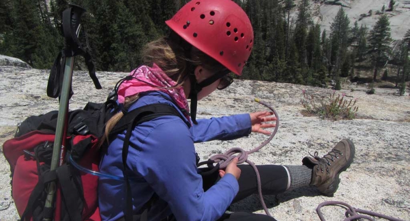 a person wearing a helmet works to tie a knot in their harness